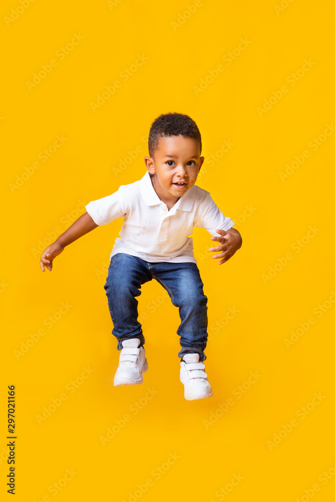 Adorable afro baby boy jumping over yellow studio background