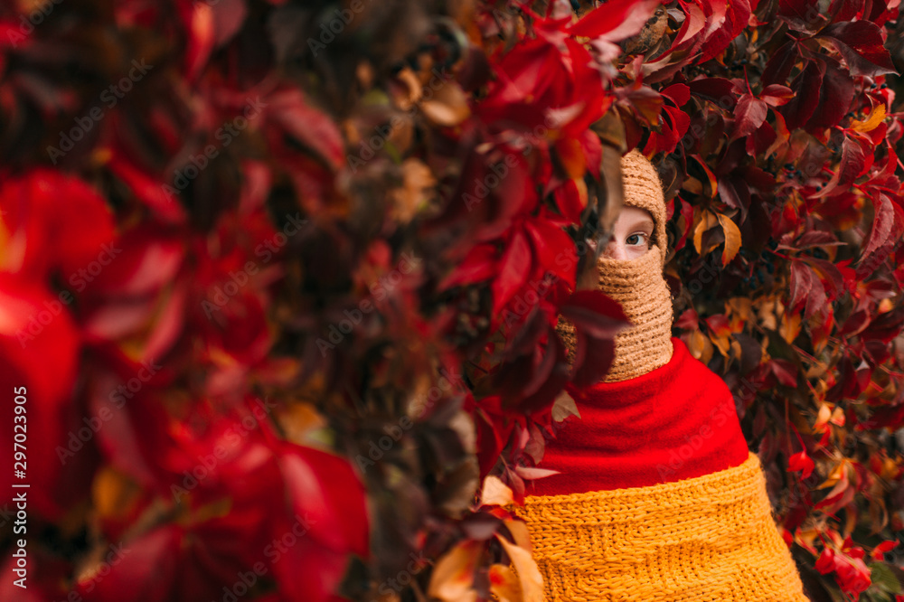 Portrait of young freckles girl wearing unusual stylish costume.  Little girl covered with three different colors scarves over ivy wall on background.