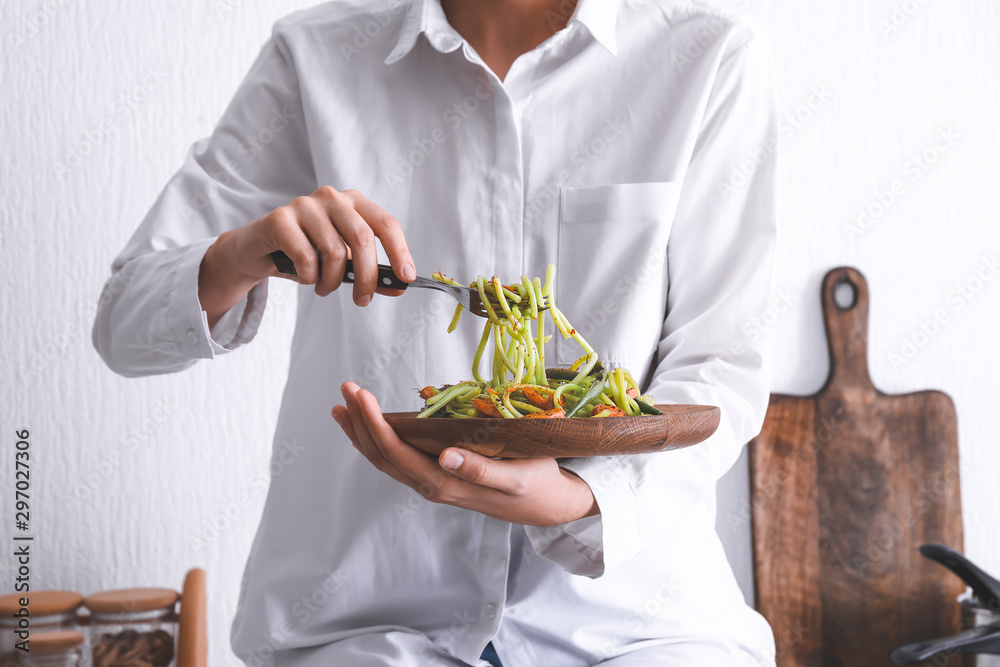 Woman eating tasty green pasta in kitchen Woman eating tasty green pasta in kitchen