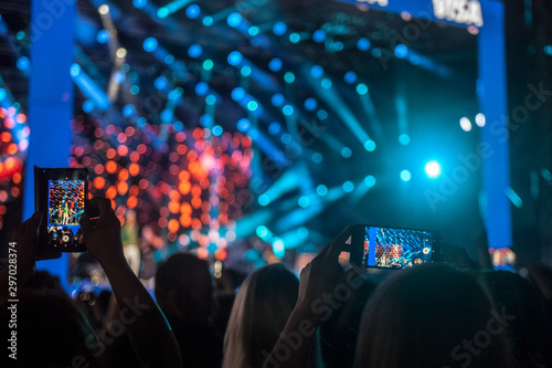 Shapes of people taking photos and videos with a smartphone telephone of a concert during a party  at night  with light and sound effects  typical from a festival