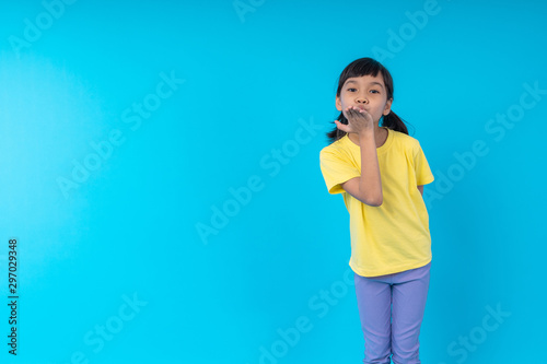 young Asia Thai girl kid in yellow shirt send a kiss on blue background in studio
