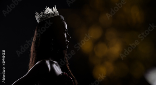 Portrait of Miss Pageant Beauty Contest in sequin Evening Ball Gown long dress with sparkle light Diamond Crown, silhouette low key exposure with curtain, studio lighting dark background dramatic