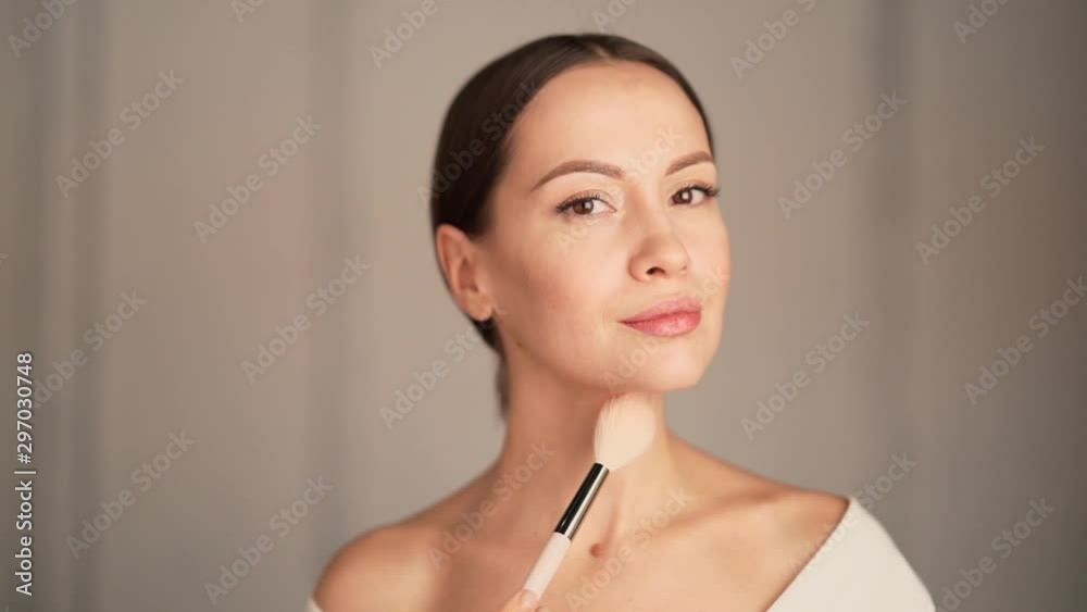 Closeup portrait of beautiful woman applying makeup with brush. Young attractive confident brunette lady on white background. Female natural beauty. Slow motion video Closeup portrait of beautiful woman applying makeup with brush. Young attractive confident brunette lady on white background. Female natural beauty. Slow motion video