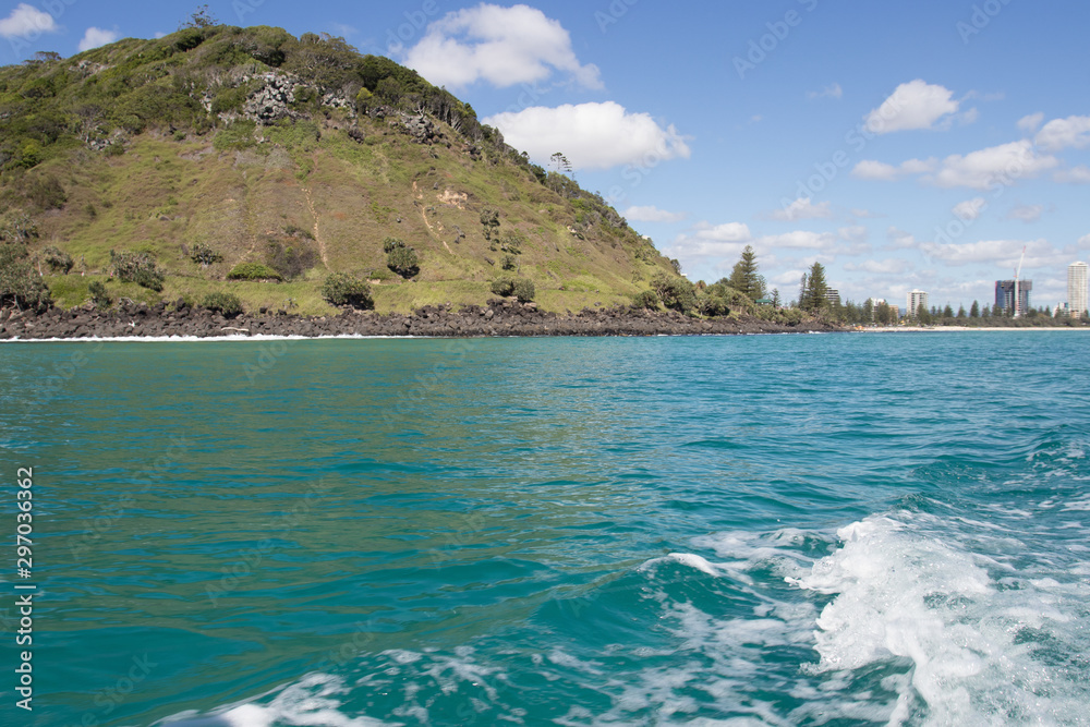 Beautiful Burleigh Headland Covered In Lush Green Grass Surrounded By Turquoise Ocean Water View From Behind A Fishing Boat