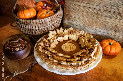 Homemade Pumpkin Pie Decorated with Pastry Cutouts of Autumn leaves with a center pumpkin, set on a wooden board with fresh pumpkins and pecans, selective focus