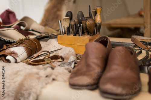 Shoemaker working desk with set of tools, ready shoes foreground and material background, selective focus photo