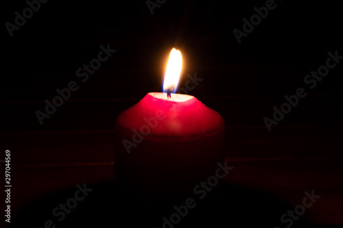 Brennende rote Kerze als Weihnachtskerze oder Weihnachtsdekoration erleuchtet die Dunkelheit und schwarze Nacht in der Adventszeit