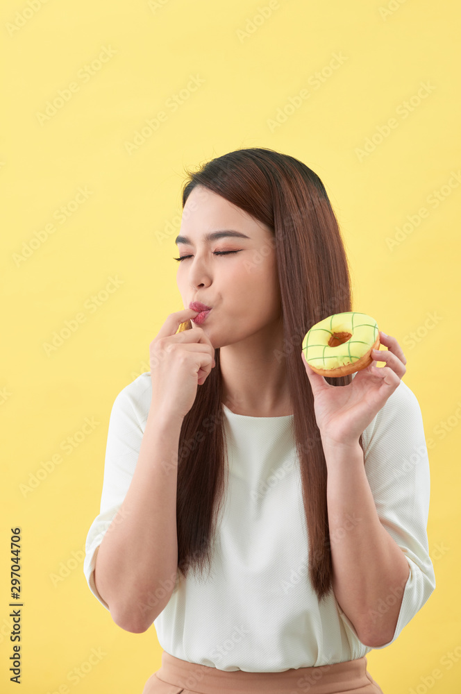 Close up portrait of a satisfied pretty girl eating donuts isolated over yellow background Close up portrait of a satisfied pretty girl eating donuts isolated over yellow background