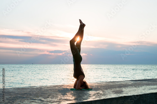 unrecognizable senoir woman with beautiful body doing yoga splits at sunrise on the sea, silhouette of yoga poses © AlexR