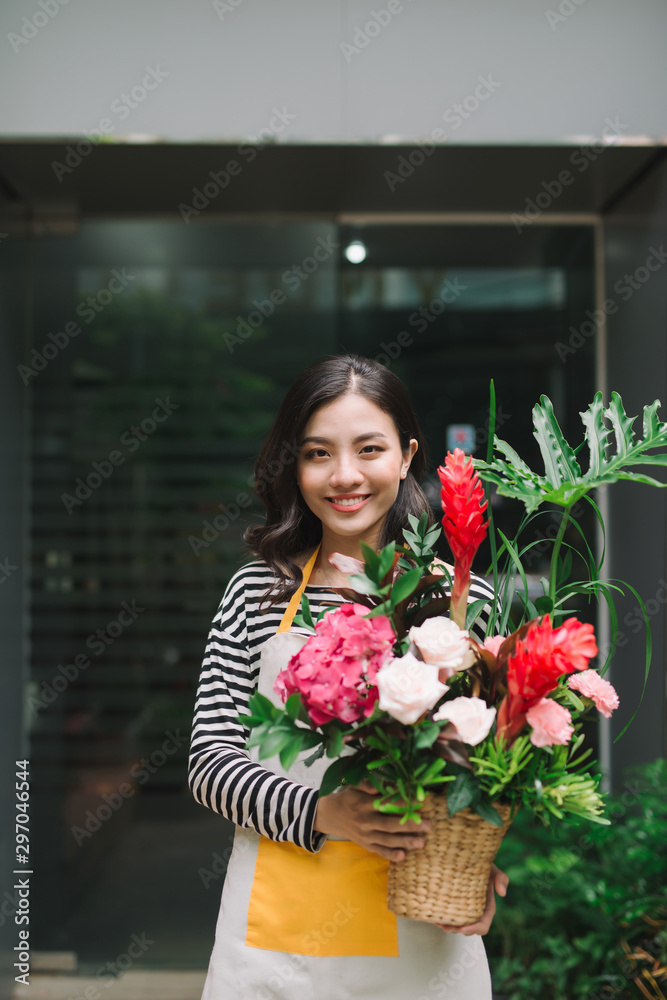 Asian woman standing in flower shop and holding bouquet of flowers