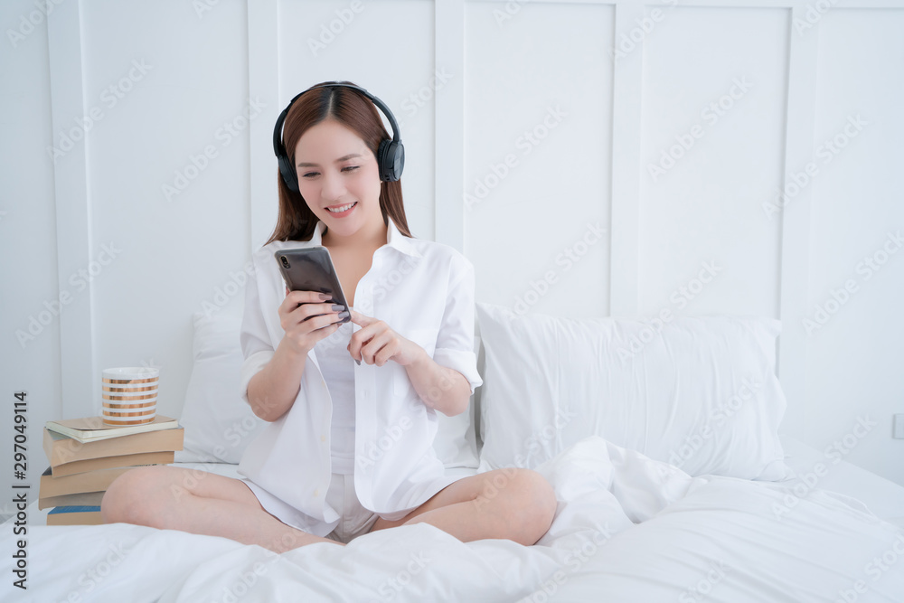 beauty asian female white dress long hair wear headphone and use type search smartphone on white bed with clam and cheerful white bedroom interior background beauty asian female white dress long hair wear headphone and use type search smartphone on white bed with clam and cheerful white bedroom interior background