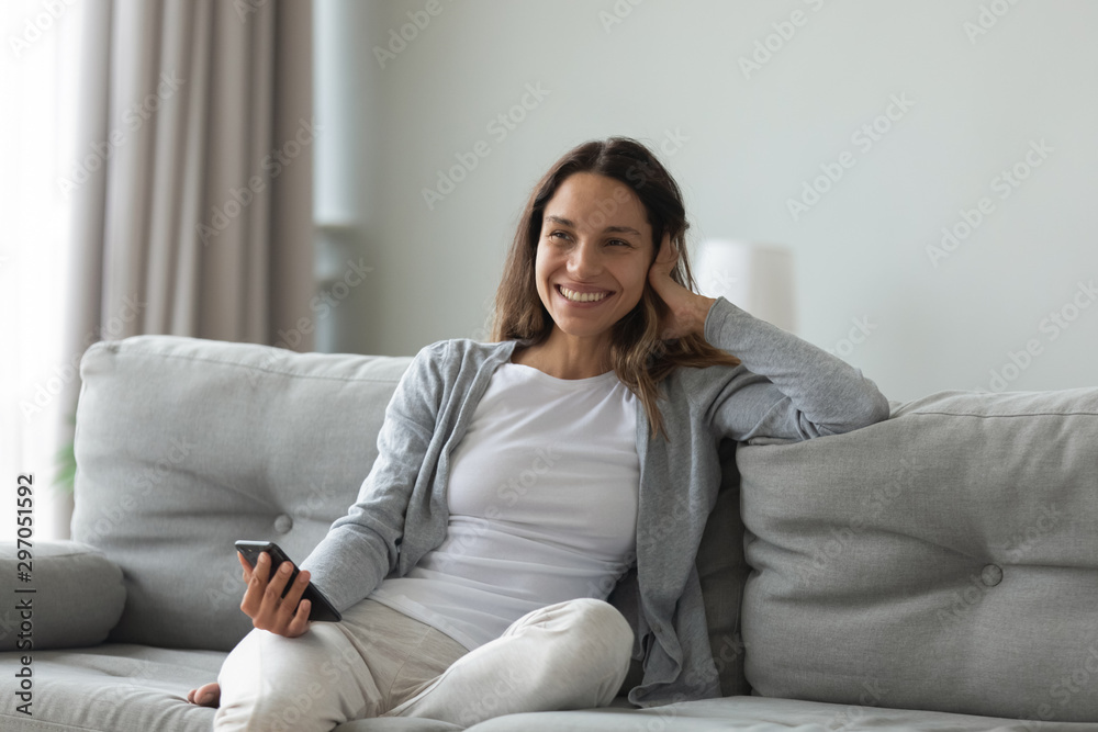 Happy woman sitting on cozy sofa with smartphone in hands.