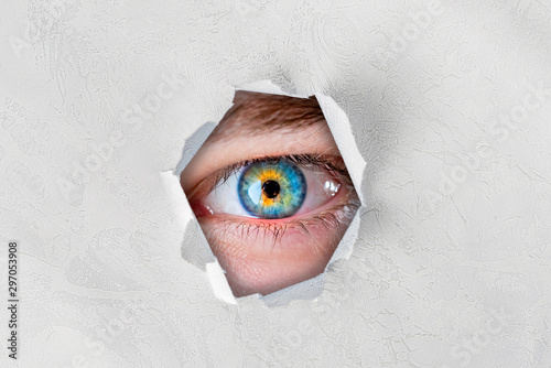 the close up of eye looking through the torn paper hole