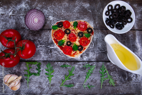 Heart shaped pizza ingredients. The name of the pizza is written in arugula.