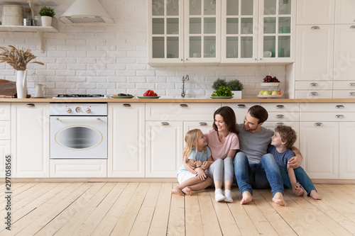Happy family with children sitting on floor in modern kitchen