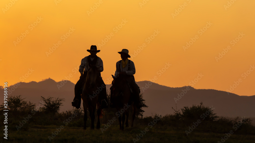 Close-up two  of Cowboys riding horses at sunset.