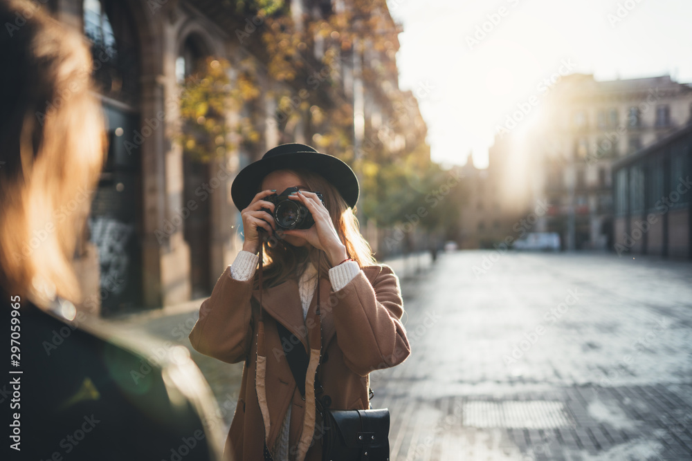Blogger photoshoot concept. Photographer with camera take photo model girlfriend. Tourist smiling girl travels in Barcelona holiday with traveler friend. Sunlight flare street in europe city - obrazy, fototapety, plakaty 