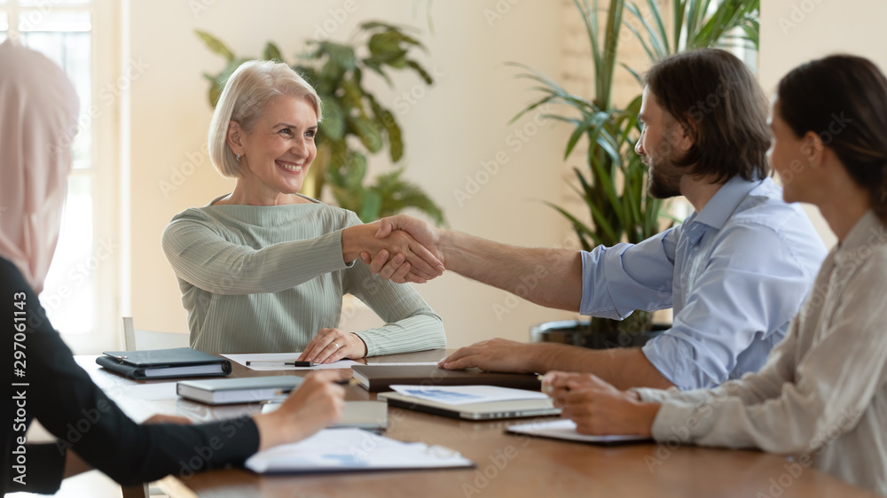 Smiling mature female leader handshake male partner at team meeting Smiling mature female leader handshake male partner at team meeting