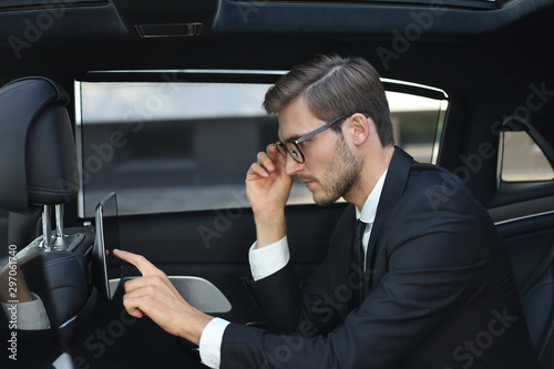 Thoughtful young businessman sitting in the luxe car and using his tablet. © ty