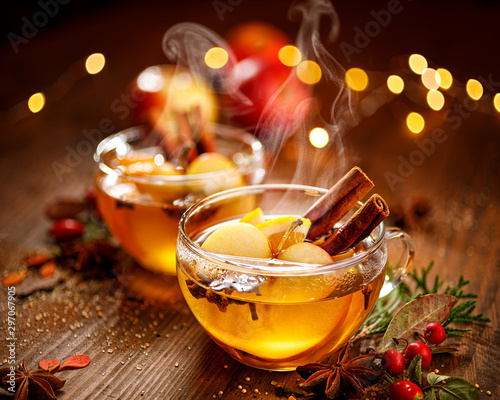 Fotografie Mulled cider with apple slices, cinnamon, cloves, anise stars and citrus fruits in glass cups on a wooden rustic table