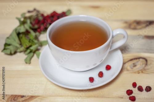 White cup of tea with plate and dry rowan berries horizontal wooden background