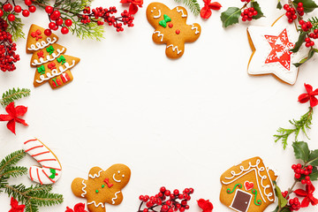 Christmas background with gingerbread cookies and branches of holly with red berries on white. Winter festive nature concept. Flat lay, copy space.