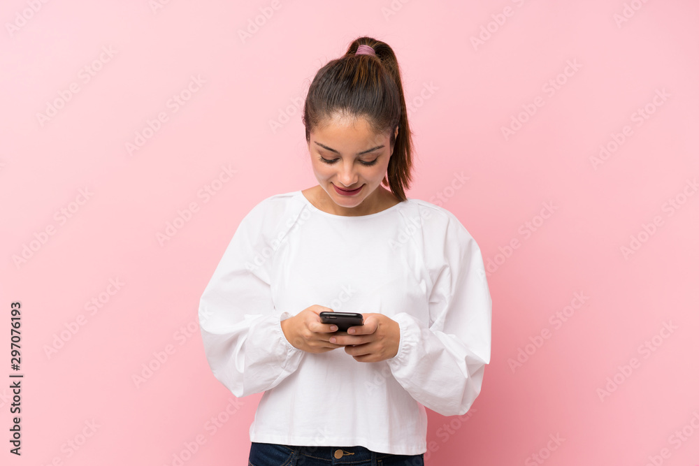 Young brunette girl over isolated pink background sending a message with the mobile Young brunette girl over isolated pink background sending a message with the mobile