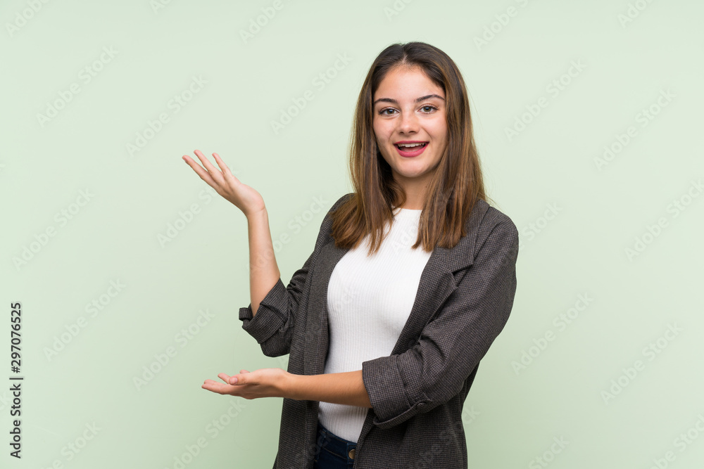 Young brunette girl with blazer over isolated green background extending hands to the side for inviting to come Young brunette girl with blazer over isolated green background extending hands to the side for inviting to come