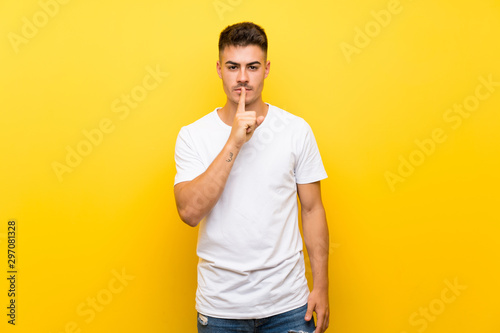 Young handsome man over isolated yellow background showing a sign of silence gesture putting finger in mouth