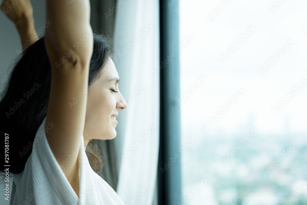 A beautiful woman wearing a towel and a white bathrobe with happy and relaxing on the bed at a condominium in the morning.