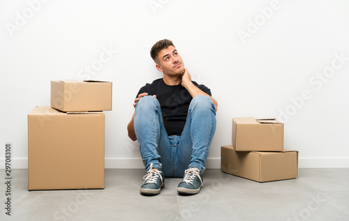 Handsome young man moving in new home among boxes thinking an idea