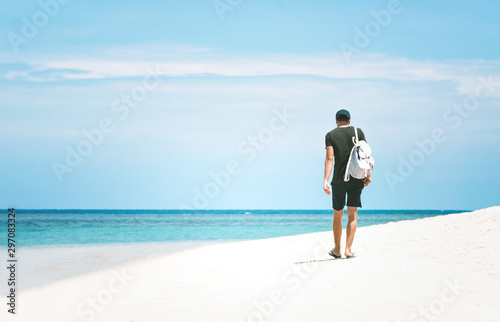 Young man with a backpack walking away along the sea shore