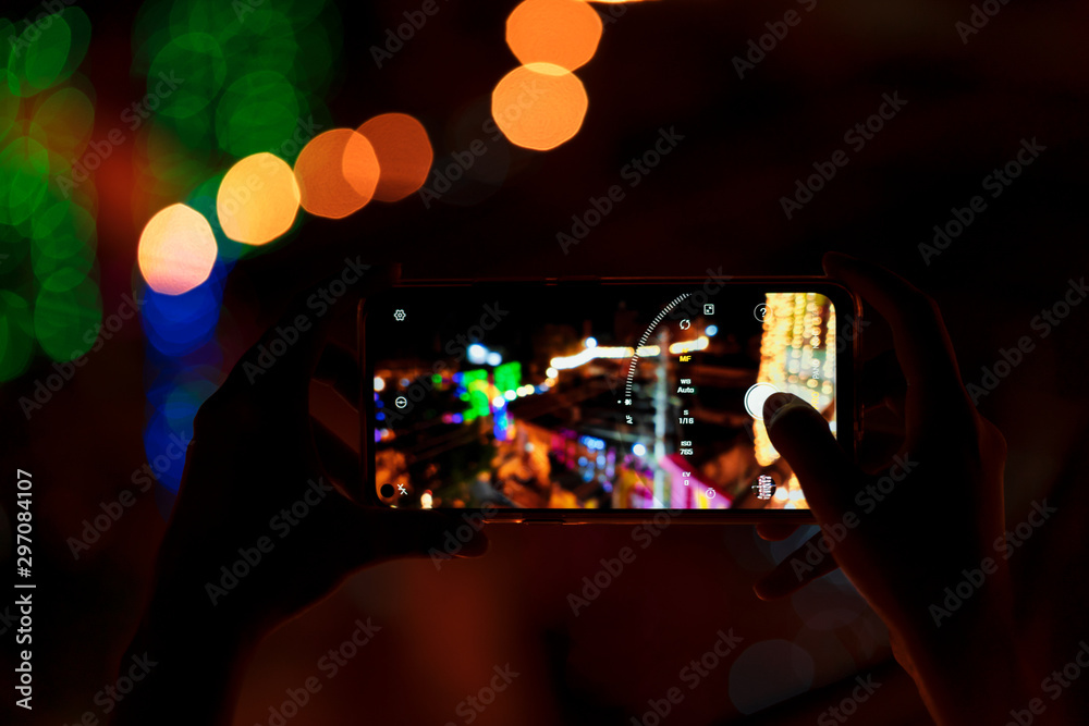 Person Taking Photo Of Diwali Decorations. Person holding smart phone & capturing photo of festive decorations at night. Background image for street mobile photography, Diwali celebration, festivals.
