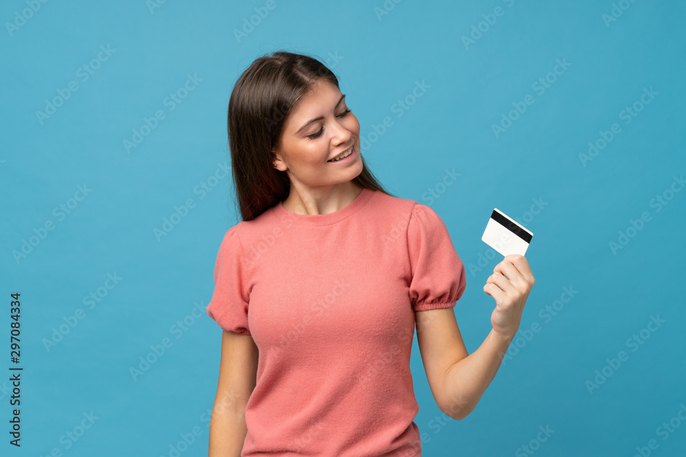 Young woman over isolated blue background holding a credit card Young woman over isolated blue background holding a credit card