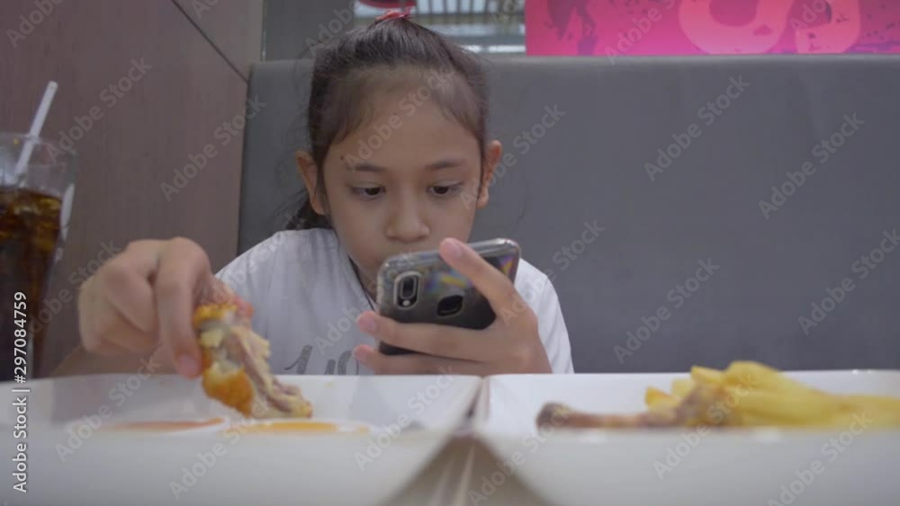 Asian cute girl eating food while using mobile phone during lunch.