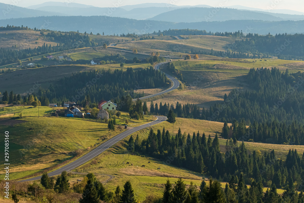 A winding long road along the foothills. Several small houses.  High mountains in the background. Autumn landscape. Panoramic view.