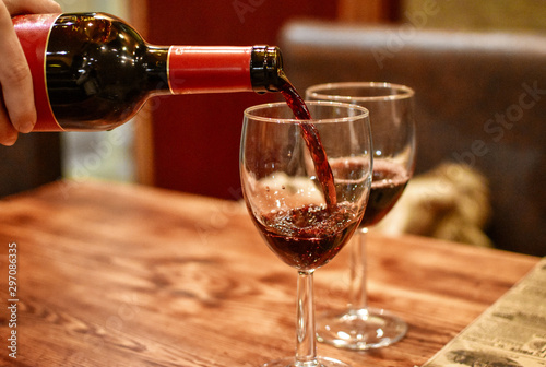 Red wine being poured into shiny wine glasses standing on wooden table. Restaurant in Pas de la Casa, Andorra -Image