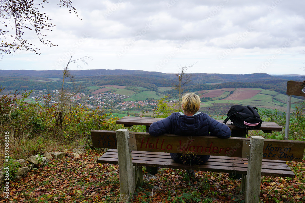 A woman is sitting on a bench enjoying the view of Freden - eine junge Frau sitzt auf einer Bank und genießt die Aussicht auf Freden