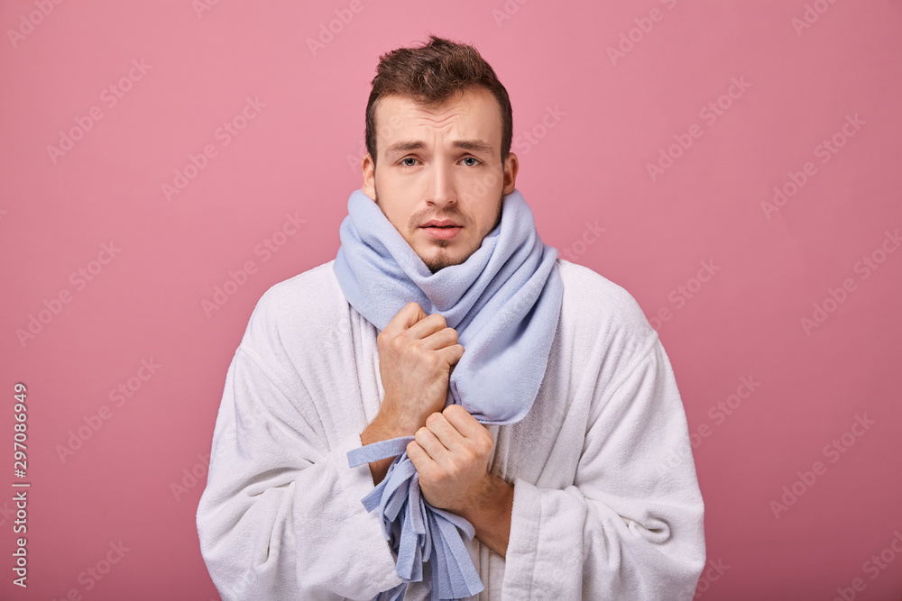 A man in a blue scarf and snow-white coat with a look of a patient is frozen and trembling, pink background. Hands are hidden under a scarf, chills, recovery, patient, sick. Recovering, getting sick. A man in a blue scarf and snow-white coat with a look of a patient is frozen and trembling, pink background. Hands are hidden under a scarf, chills, recovery, patient, sick. Recovering, getting sick.