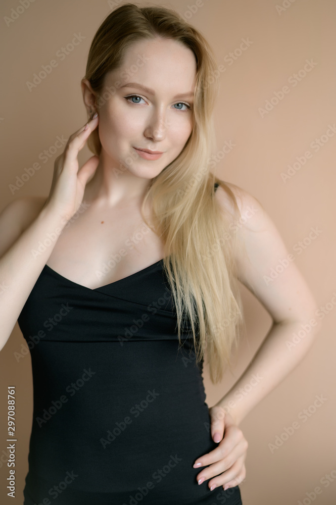 Graceful young woman in a black top posing against beige wall. Graceful young woman in a black top posing against beige wall.