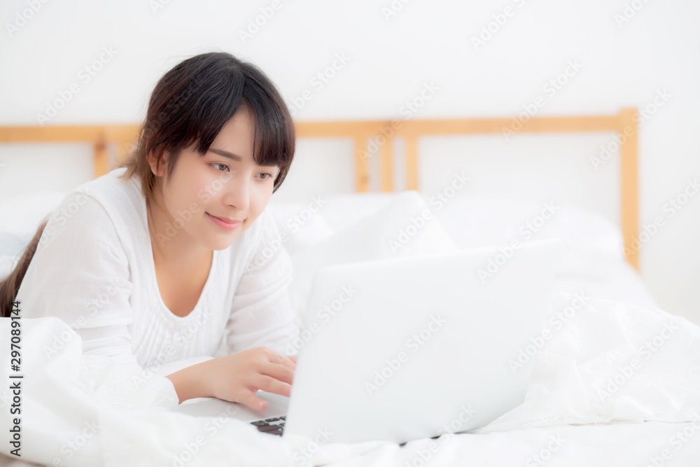 Beautiful portrait asian young woman smile lying on bed using laptop computer with happy at bedroom for leisure and relax, freelance with girl working notebook, communication concept. Beautiful portrait asian young woman smile lying on bed using laptop computer with happy at bedroom for leisure and relax, freelance with girl working notebook, communication concept.