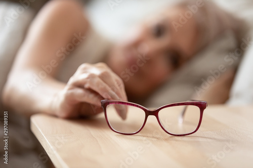 Obraz na płótnie Older mature woman taking optical glasses from bedside table