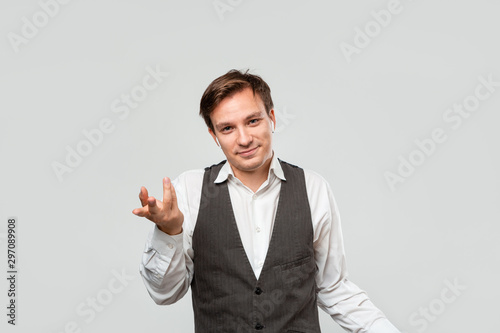 фотографія Young businessman in a white shirt and grey vest is at lost shrugging his shoulders isolated over grey background