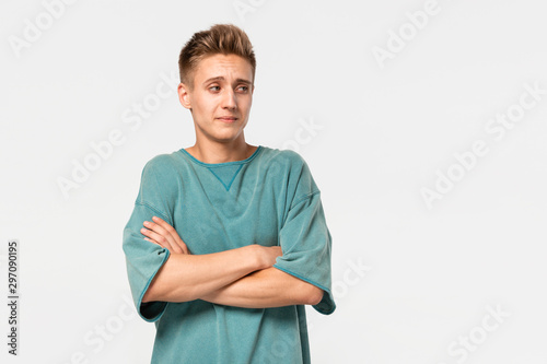 Unsure young man in a green tee holds hands folded isolated over grey background. © ianachyrva