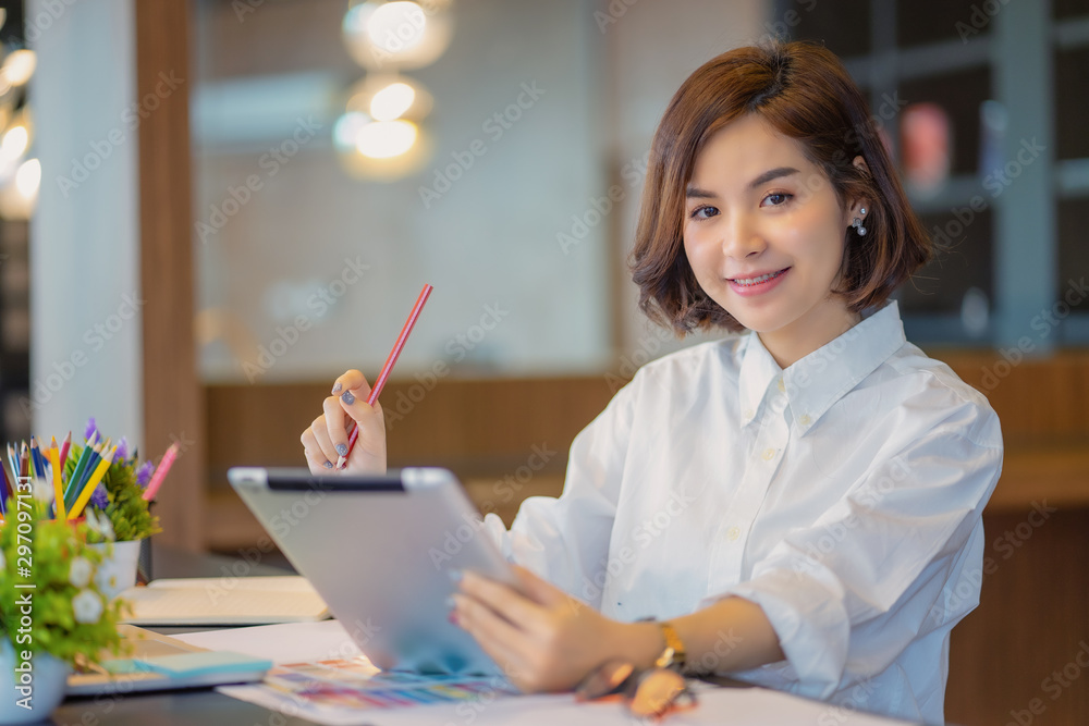 Young beautiful asian woman in white shirt holding pencil while looking at tablet Young beautiful asian woman in white shirt holding pencil while looking at tablet