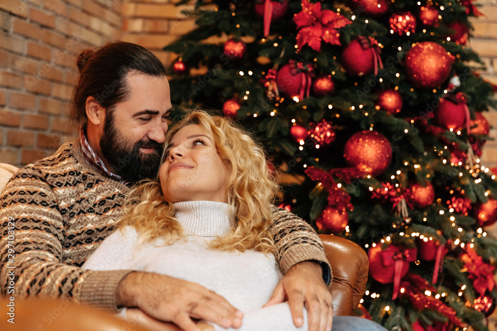 Christmas. Couple. Home. Togetherness. Man and woman are hugging and smiling near the Christmas tree Christmas. Couple. Home. Togetherness. Man and woman are hugging and smiling near the Christmas tree