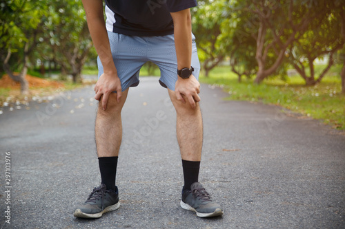 Male runner athlete knee injury and pain. Man suffering from painful knee while running in the public park.