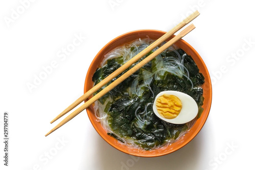 Wakame seaweed soup, clear noodles and egg in a round brown plate on a white background. Asian food for vegetarians. A healthy diet
