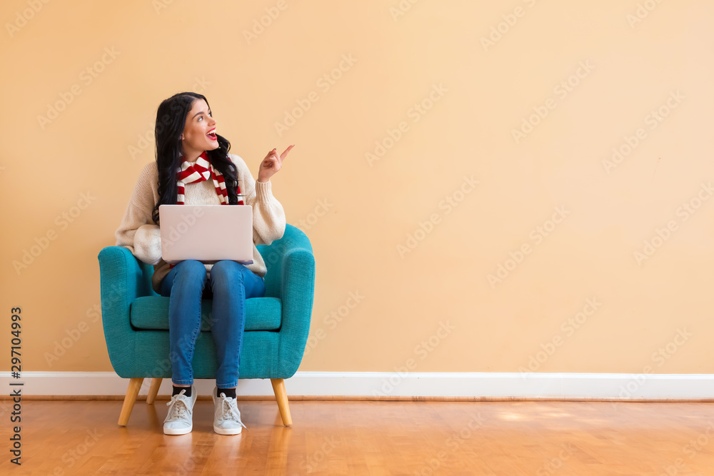 Young woman with a laptop computer in a thoughtful pose sitting in a chair - obrazy, fototapety, plakaty 