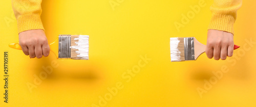 Paint brush in the hand of a girl on a yellow background, concept of apartment repair and painting works. Panoramic mockup with space for text photo